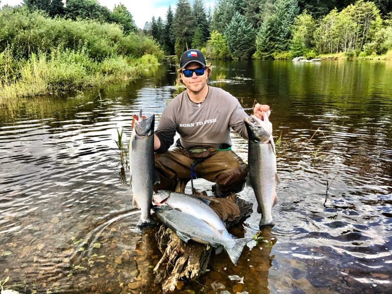 Fisherman holding three salmon in pristine Alaska river