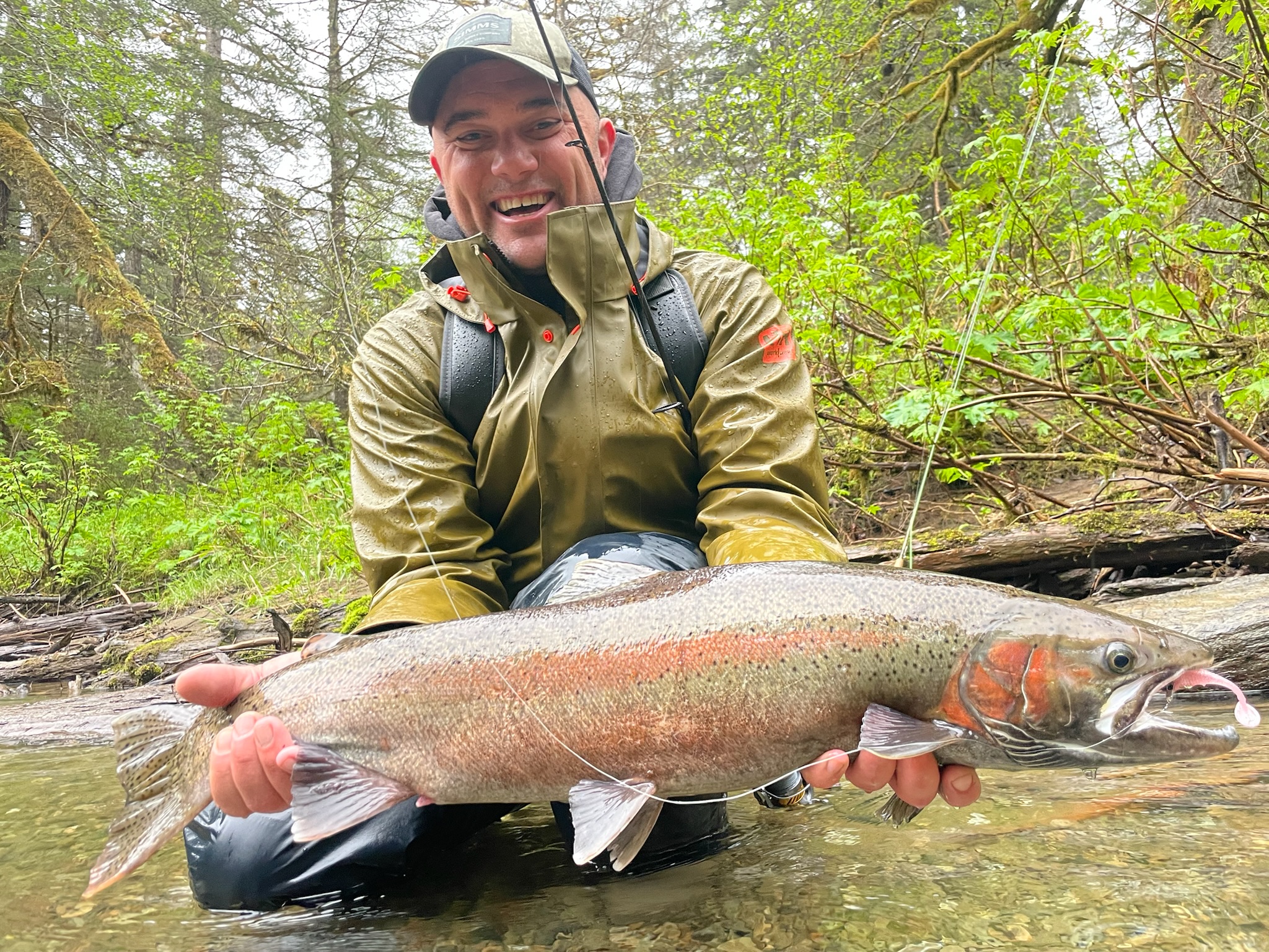 Smiling angler with rainbow trout in forest stream