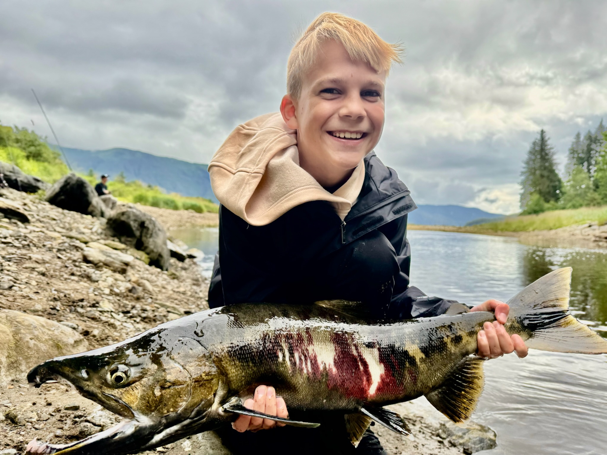 Young boy with salmon catch on rocky riverbank