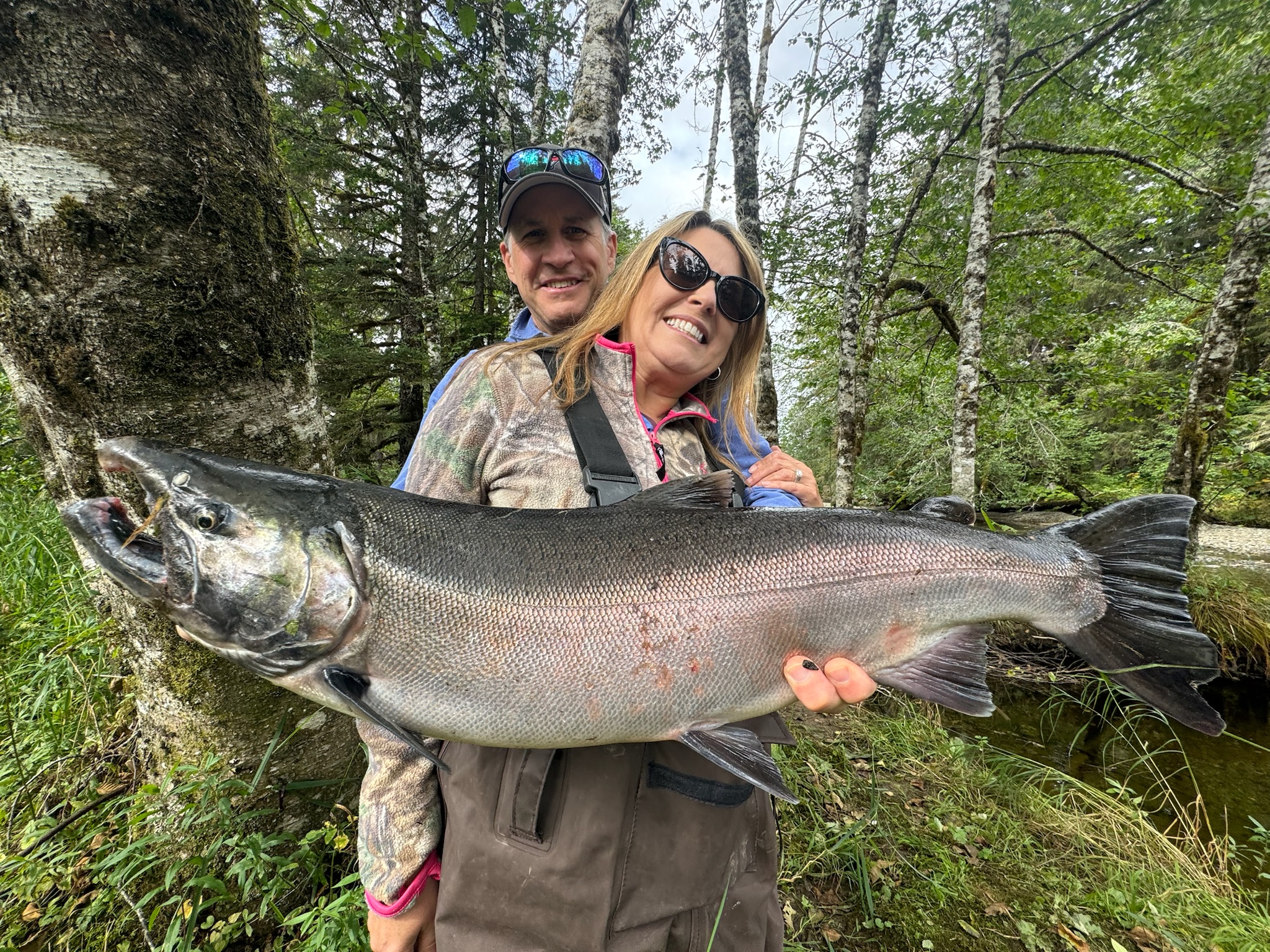 Couple holding salmon in forest stream Alaska